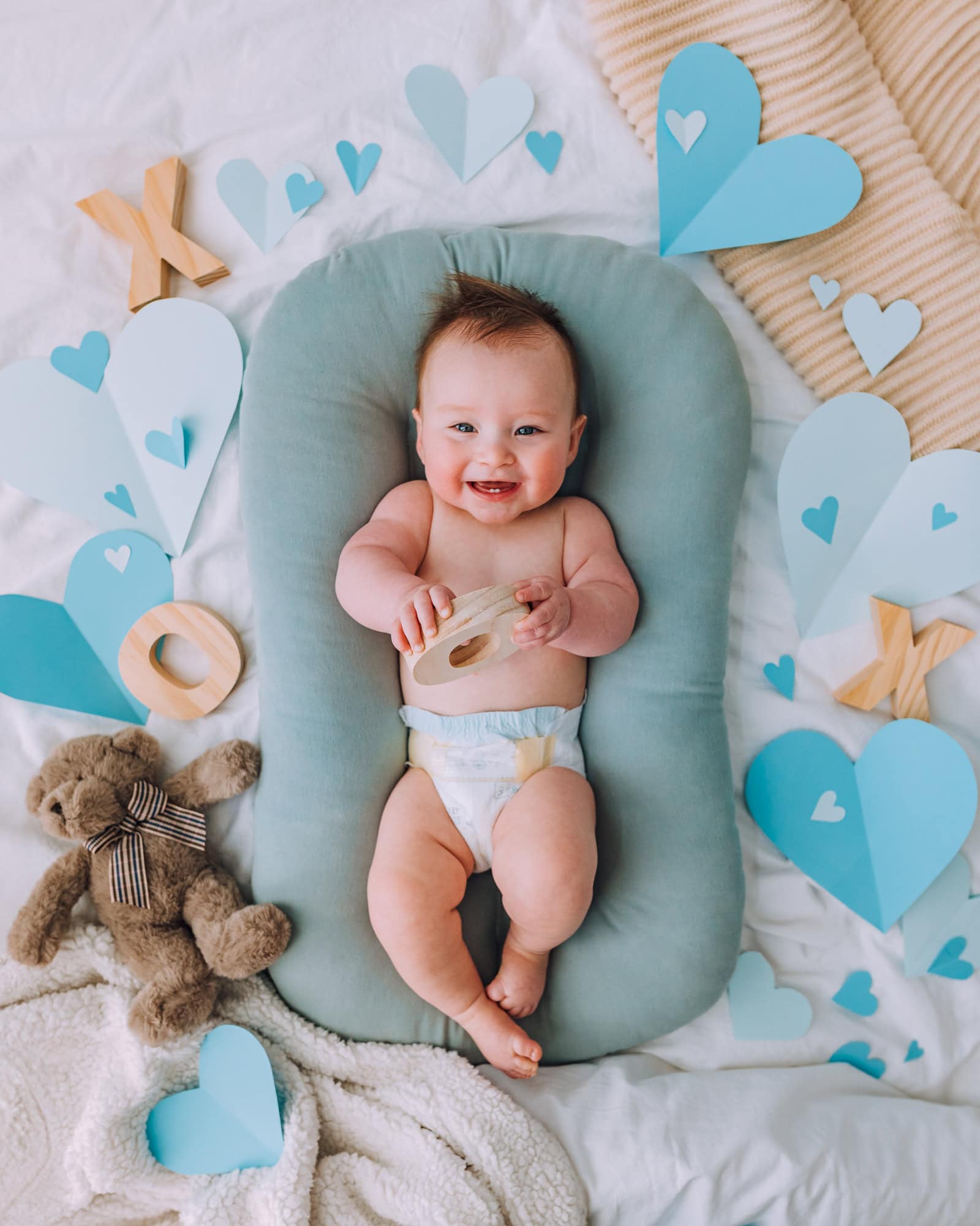 valentine's day baby photoshoot with baby lying in snuggle me organic baby lounger surrounded by paper hearts and a teddy bear